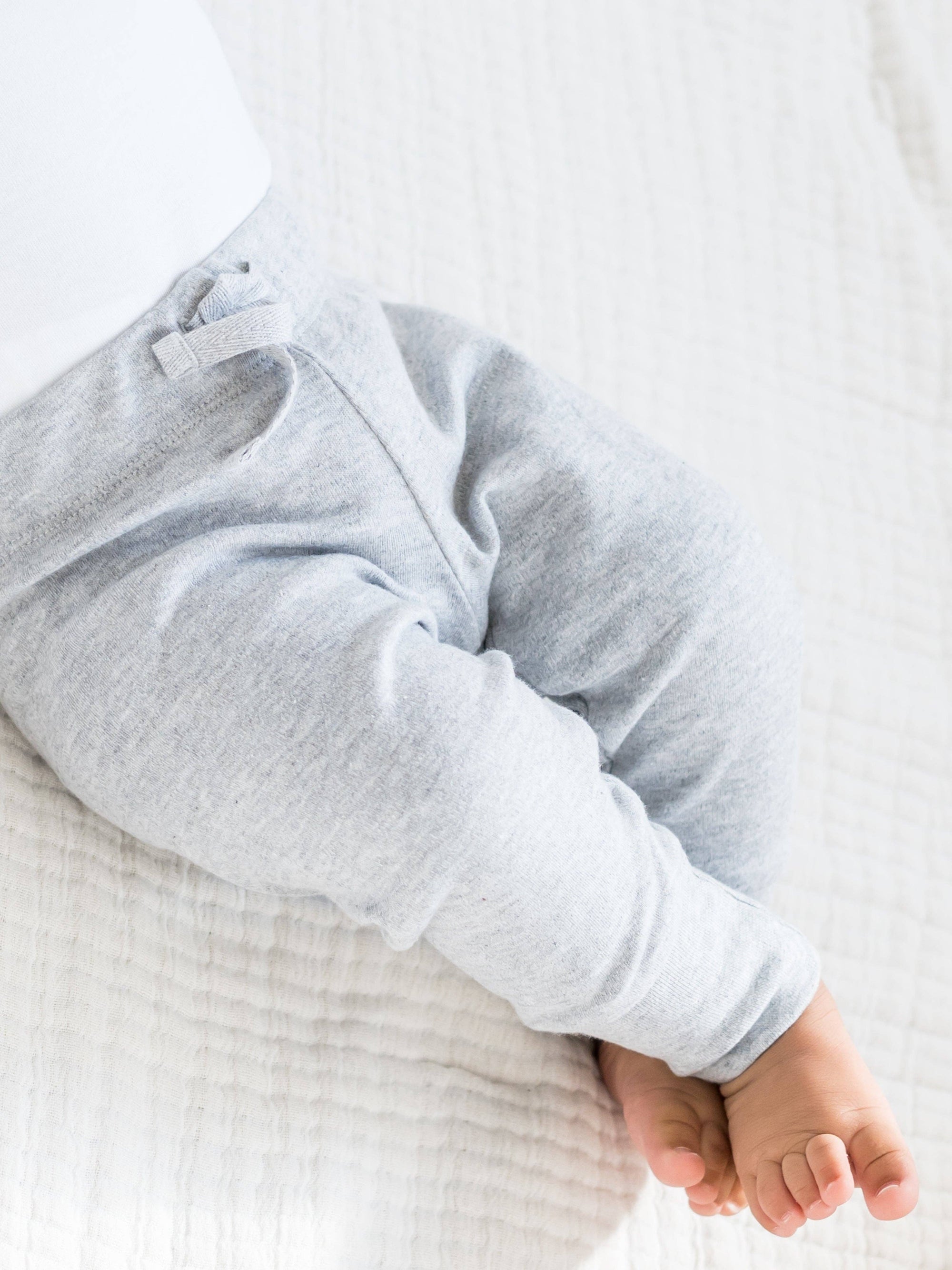 Close-up of a baby's legs in light gray pants on a white background