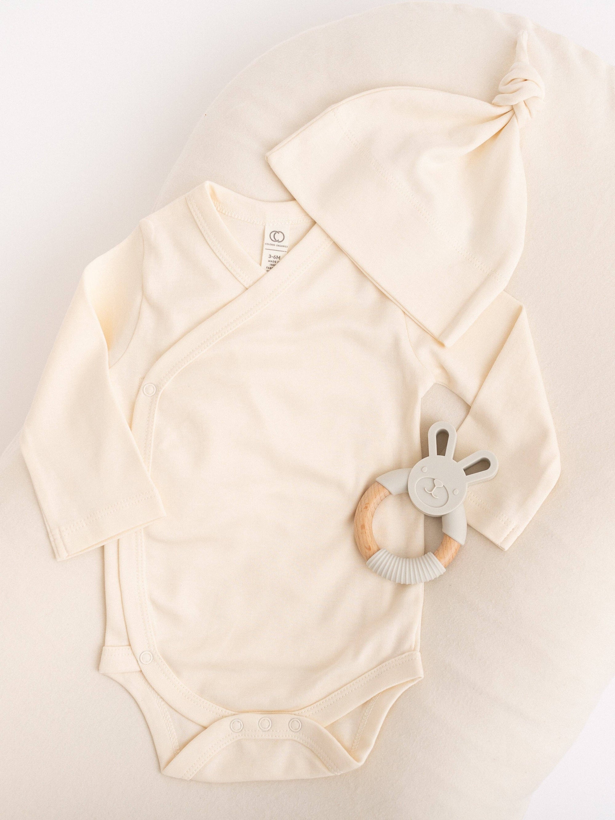 Beige baby onesie with a soft toy on a light background