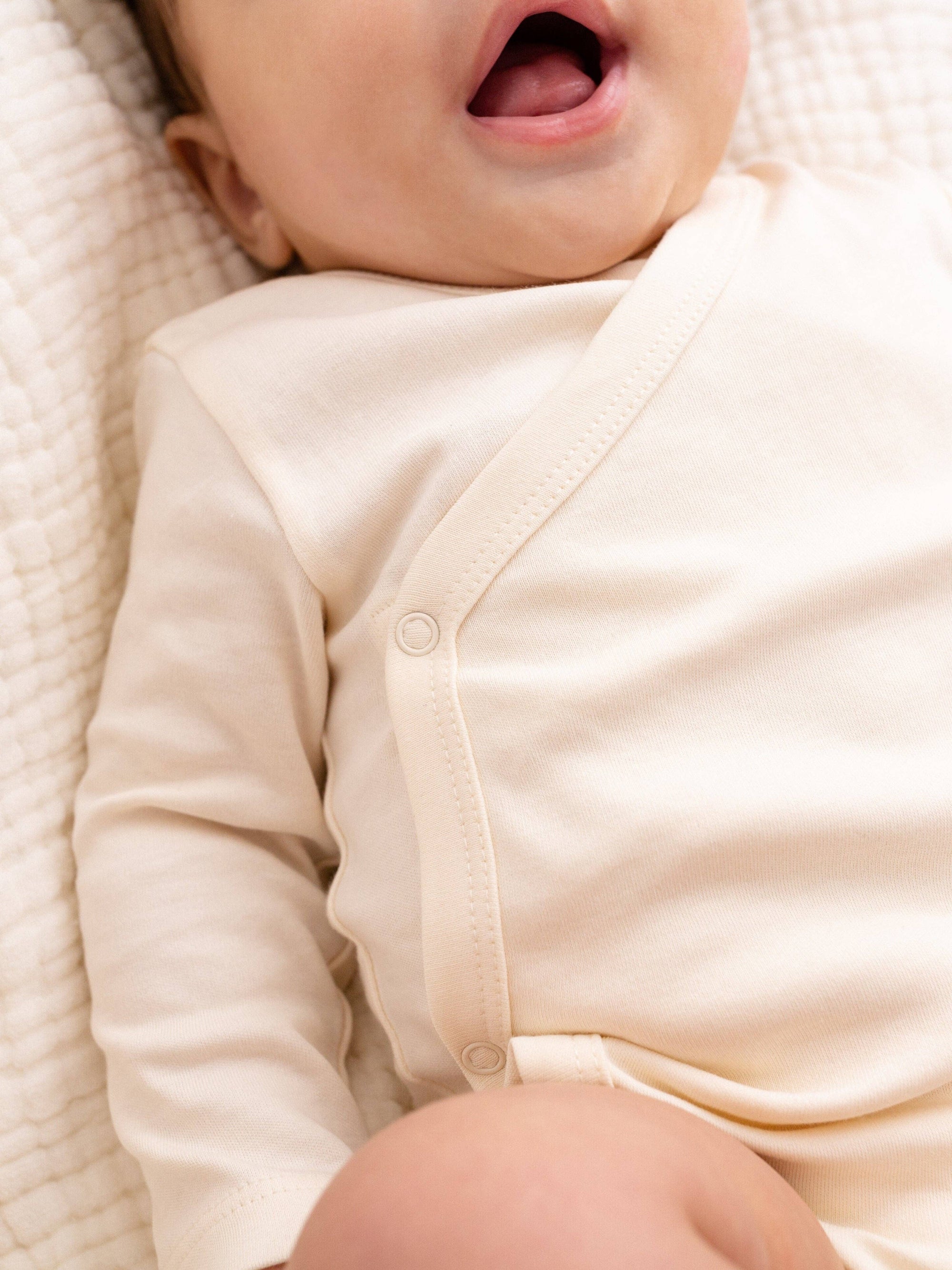 Close-up of a baby in a cream-colored outfit lying on a textured surface