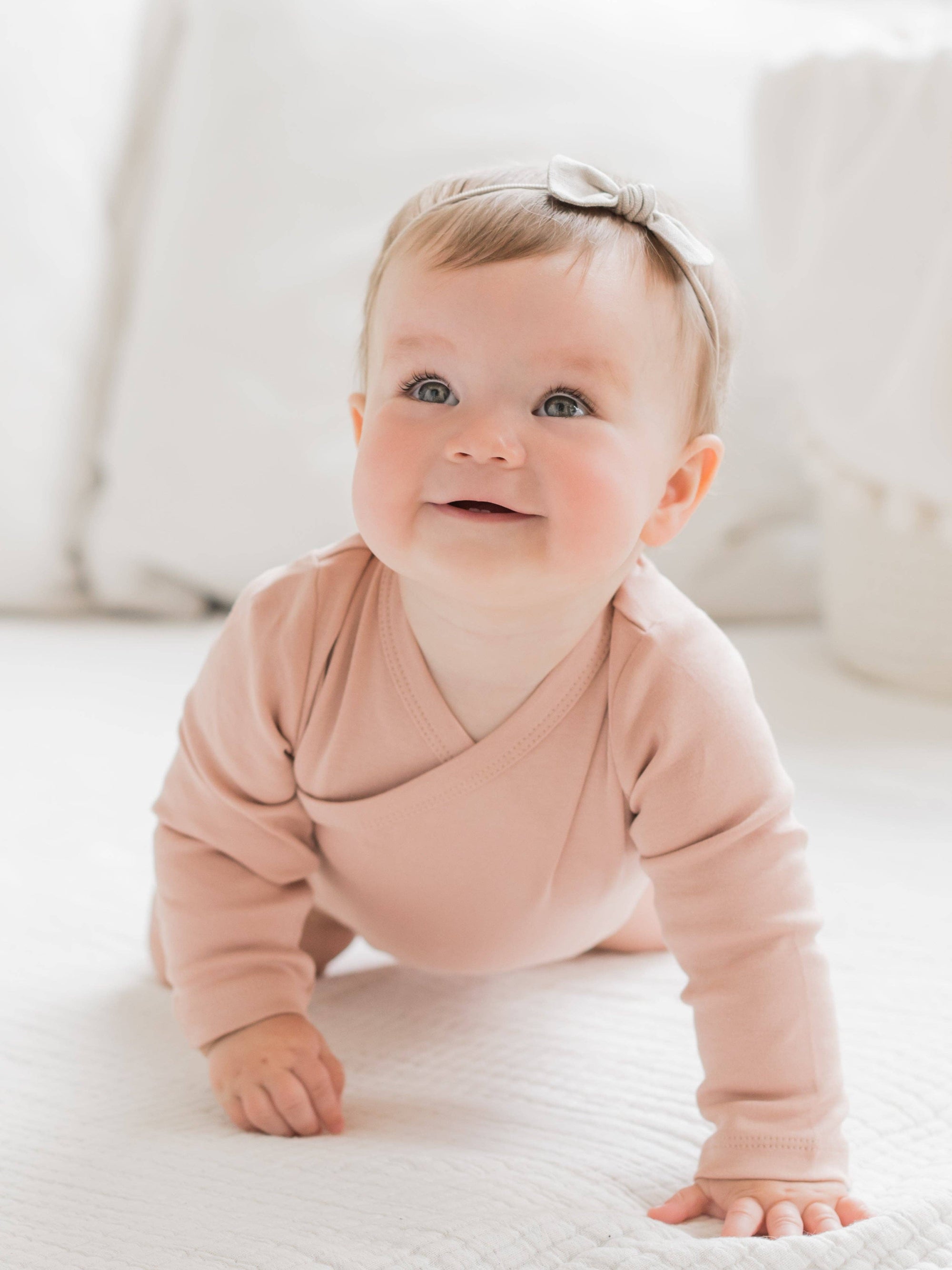 Baby in a pink onesie crawling on a white surface
